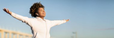 Genç siyahi bayan koşucu kollarını açıyor ve açık havada antrenman yaparken temiz hava soluyor, gülümseyen Afro-Amerikan kadın spor kıyafetleriyle dışarıda spor yapıyor, boşluğu kopyalıyor.