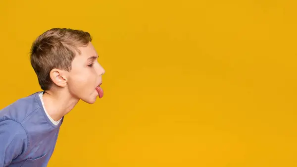 stock image Little boy teasing someone, showing tongue and making face at free space aside, orange background