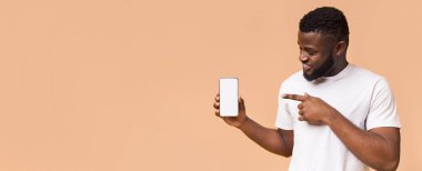 Kısa siyah saçlı, sakallı ve beyaz tişörtlü genç bir Afrikalı Amerikalı şeftali arka planda duruyor. Elinde boş beyaz ekranlı akıllı bir telefon var, kopyalama alanı.