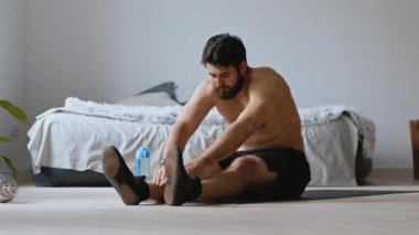 Esneklik eğitimi. Genç adam esneme egzersizi yapıyor, evde yerde oturuyor.
