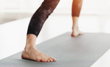 Yoga minderinin üzerinde kendinden emin bir şekilde duran, yoga pratiği yaparken denge ve duruşa odaklanan bir kadın bacağı yakın plan çekimi.