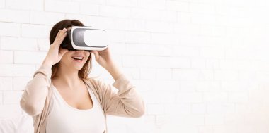 Genç bir kadın sanal gerçeklik kulaklığı kullanıyor ve parlak bir odada gülümsüyor. Dijital deneyimin tadını çıkarıyor gibi görünüyor..