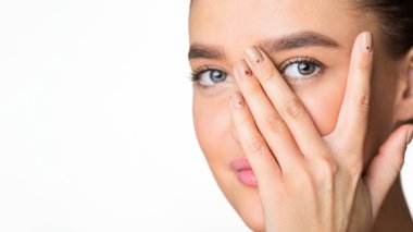 Bu fotoğrafta bir kadın elleriyle gözlerini kapatıyor. Elleri gözlerinin üstüne konmuş, ışığı engelliyor ve muhtemelen kendini bir şeyden koruyor, uzayı kopyalıyor.