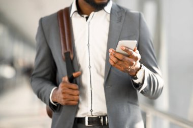 Afro-Amerikalı bir adam havaalanı terminalinde telefonunu kullanıyor, bavulunun yanında duruyor. Ayarlar modern ve hareketli, etkin bir seyahat, kesilmiş