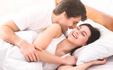 Genç bir çift yatakta uzanıyor, sarılıyor ve gülüyor. İlişkilerindeki neşe ve mutluluğu göstermek için yakın ve samimi bir anı paylaşıyorlar..