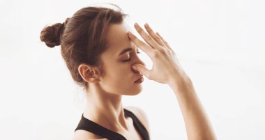 Görüntüde bir kadın gösteriliyor, eli yüzüne doğru kalkıyor. Ağzına ya da yanağına dokunuyor ya da örtüyor gibi görünüyor. Eline ve yüz ifadesine odaklanmış durumda..