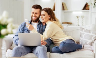 İnternette sörf yapıyorum. Genç Çift Laptop ve Smartphone ile Rahatlatıcı, Kanepede Oturan