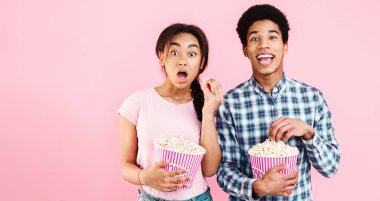 Patlamış mısır yemek, pembe bir arka plan üzerinde film izlerken şok Afrikalı-Amerikalı Çift