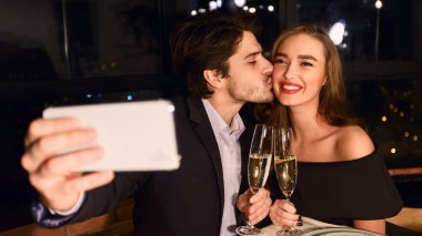 Çift yapma selfie fotoğraf akıllı telefon ile restoranda romantik bir akşam yemeği sırasında öpüşme portre