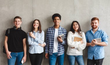 Kitap ile üniversite öğrencileri gri duvar üzerinde kameraya gülümseyerek, mola sahip