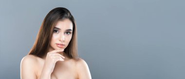 Elini nazikçe çenesine koyup poz veren çıplak bir kadın düşünceli bir yüz ifadesi sergiliyor.