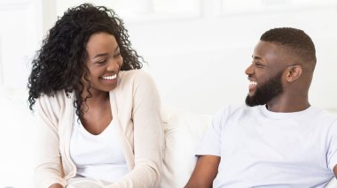 Mutlu bir çift, ışık dolu bir odada kanepede birlikte oturur. İkisi de gülümsüyor ve birbirlerine bakıyorlar..