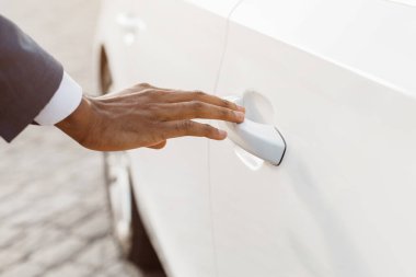 Beyaz bir arabanın kapı koluna uzanan bir elin yakın plan görüntüsü. El ön planda, araba kapısı da arka planda. El kapı koluna uzanıyor.