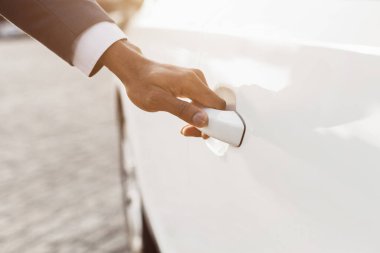 Beyaz bir arabanın kapısını açan bir insan elinin yakın plan görüntüsü. Güneş ışığı arabanın üzerinde ışıl ışıl parlıyor..