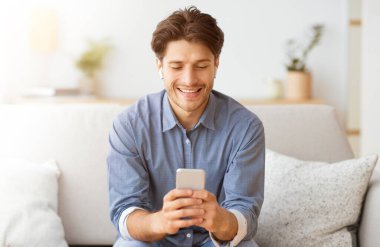 Bir adam koltukta otururken telefonuna bakarken gülümsüyor..