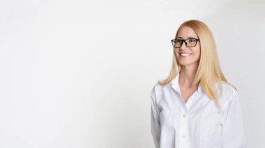 Siyah çerçeveli gözlük takan ve beyaz gömlekli gülümseyen sarışın bir kadın beyaz arka planda duruyor. Neşeli bir ifadeyle yan tarafa bakıyor, boşluğu kopyala