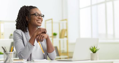 Neşeli Afrikalı Amerikalı iş kadını bilgisayarını modern ofis ortamında kullanıyor.