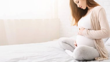 Anne ve doğmamış çocuk bağlantısı. Güzel hamile kadın karnına okşayarak, Bebek konuşurken, evde yatakta oturan, kopya alanı