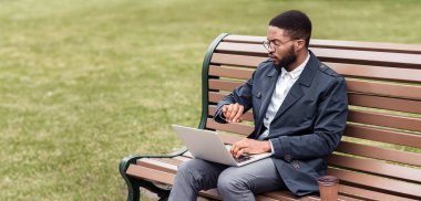 Siyah işadamı, yanında bisikletiyle bir bankta oturuyor. Atmosfer rahat ve verimli, doğa ve teknolojinin bir karışımını sergiliyor..