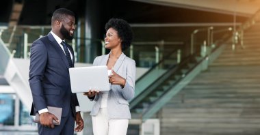 Genç Afrikalı kadın meslektaşı ile açık havada dururken dizüstü ekrana parmak işaret