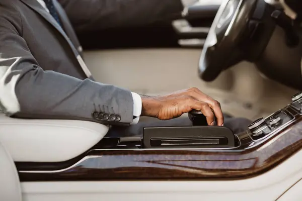 stock image Mans hand resting on the gear shift of a car. The hand is wearing a suit and is in a relaxed position. Interior of the car is visible in the background, with a white leather seat and dark wood trim.