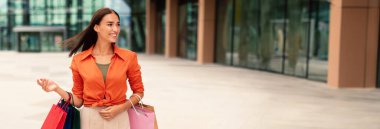 Moda yaşam tarzı. Açık havada alışveriş yapan alışveriş torbalarıyla poz veren mutlu genç bayan müşteri, şehirde yürüyüş ve alışveriş yapmaktan hoşlanıyor, mesaj atmak için boş yere bakıyor