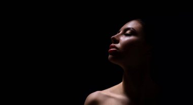 Karanlık bir ortamda yakalanan bir kadının yakın plan fotoğrafı. Kadın yukarı bakıyor ve yüzü tek bir ışık kaynağı tarafından aydınlatılıyor. Yüzünde gölgeler beliriyor..