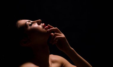 Görüntü, karanlık bir odadaki tek bir ışık kaynağı tarafından aydınlatılmış bir kadının yakın çekimini gösteriyor. Gözleri kapalı ve dudakları hafifçe ayrılmış, bir yakınlık ve hassasiyet hissi yaratıyor.