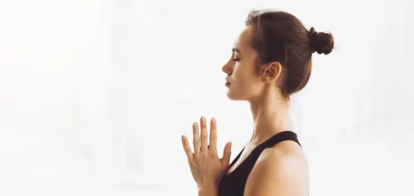 stock image A woman is standing in a yoga pose, with her hands pressed together in front of her chest. She is balanced on one leg, with the other raised behind her, panorama with copy space