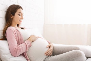 Active unborn baby pushing his mom, pregnant lady enjoying her pregnancy, lying in bed at home, copy space