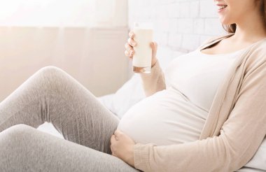 Hamilelik için faydalı bir diyet. Bin yıllık hamile bir kadın bir bardak sütle yatakta oturuyor.