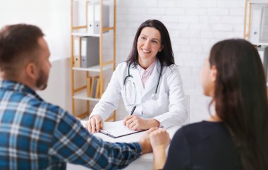 Beyaz önlüklü kadın doktor birkaç kişiyle aynı masaya oturur ve not alır. O gülümsüyor ve çifti dikkatle dinliyor gibi görünüyor. T