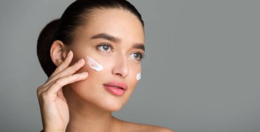 Güzel Kadın Yüz Kremi Uygulama ve Uzağa Bakıyor, Gri Stüdyo Arka Plan