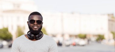 Sakallı bir adam dışarıda kulaklık ve güneş gözlüğü takarken gülümsüyor..