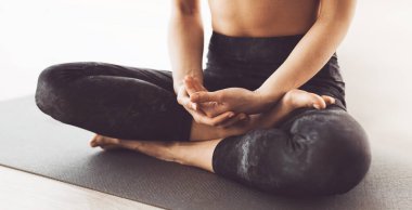 Cropped of flexible woman is engrossed in a session of yoga, demonstrating an advanced seated pose with precise hand placement on a mat. clipart