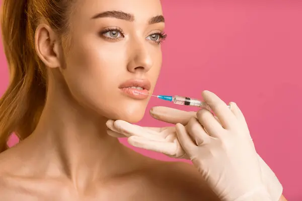 stock image A young woman with long red hair is receiving lip injections from a medical professional wearing white gloves. The woman is looking to the side and the gloved hand holding the syringe