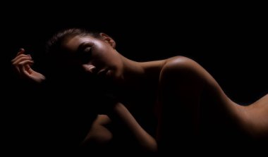 This is a photo of a woman posing in silhouette against a dark background. Her body is partially visible, with her face and shoulders illuminated by a soft light. clipart