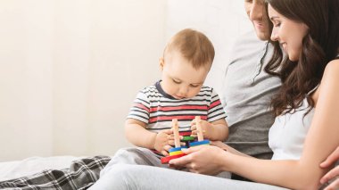 Görüntü, istifleme oyuncağıyla oynarken ailesinin kucağında oturan küçük bir çocuğu gösteriyor. Ailesi gülümsüyor ve onun oynamasını izliyor. Sahne sıcak ve samimi, sevgi dolu bir aileyi gösteriyor.