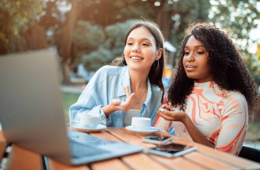 İki kadın bir kafede bir masada oturuyorlar. Bir kadın laptopa bakar ve konuşur, diğer kadın ise dikkatle dinler. İki kadının da önünde kahve fincanı var..