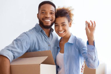 Kendi evim. Genç Afro Eşler Yeni Ev Anahtarlarını Gösteriyor Kapalı Kapılar Arasında Kucaklaşma ve Taşıma Kutusu.