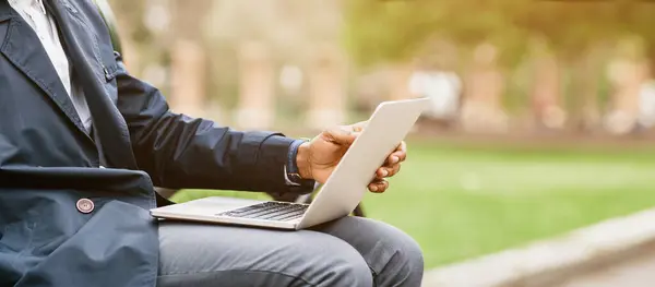 stock image A businessman is seated on a park bench, working on his laptop with his bike beside him. The scene is peaceful and productive, showing a harmonious blend of work and nature, cropped