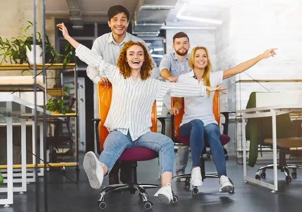 Mola zamanı. Mutlu iş arkadaşları işyerinde eğlenmek, birlikte çalışma alanında ofis sandalye yarış yapma