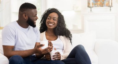 Bir çift beyaz bir kanepede oturuyor, ellerinde kahve fincanları, birbirlerine bakıp gülümsüyorlar..