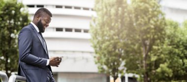 Çekici mutlu işadamı modern ofis binası yakınında cep telefonu, kopya alanı ile yan görünüm mesajlaşma olduğunu. İş, teknoloji ve iletişim konsepti