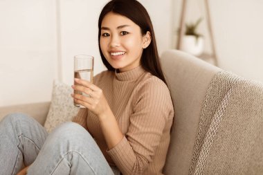 Asyalı Kız İçme Cool Su Kanepede Oturan ve Kamera Bakıyor