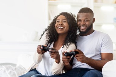 Bir çift kanepede oturmuş video oyunları oynarken gülüyor..
