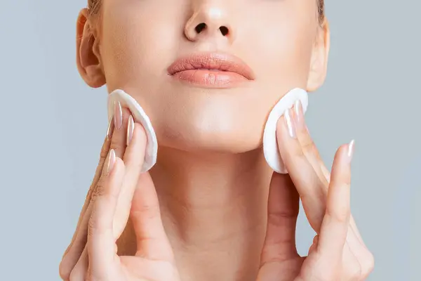 stock image This image shows a woman applying cotton rounds to her face as part of her skincare routine. She is using the cotton rounds to cleanse or tone her skin, cropped