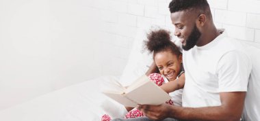 Afrikalı bir Amerikalı baba kanepeye oturur ve kızına kitap okur. Küçük kız babasının kucağında oturuyor ve gülüyor. Baba gülümsüyor ve anın tadını çıkarıyor gibi görünüyor.