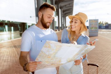 Yeni evli çiftimiz harita kullanarak ve gezmek için turistik yerleri arayarak havaalanına varıyor.