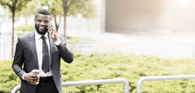 Neşeli Afrikalı Amerikalı iş adamı cep telefonuyla konuşuyor kahve molası veriyor.